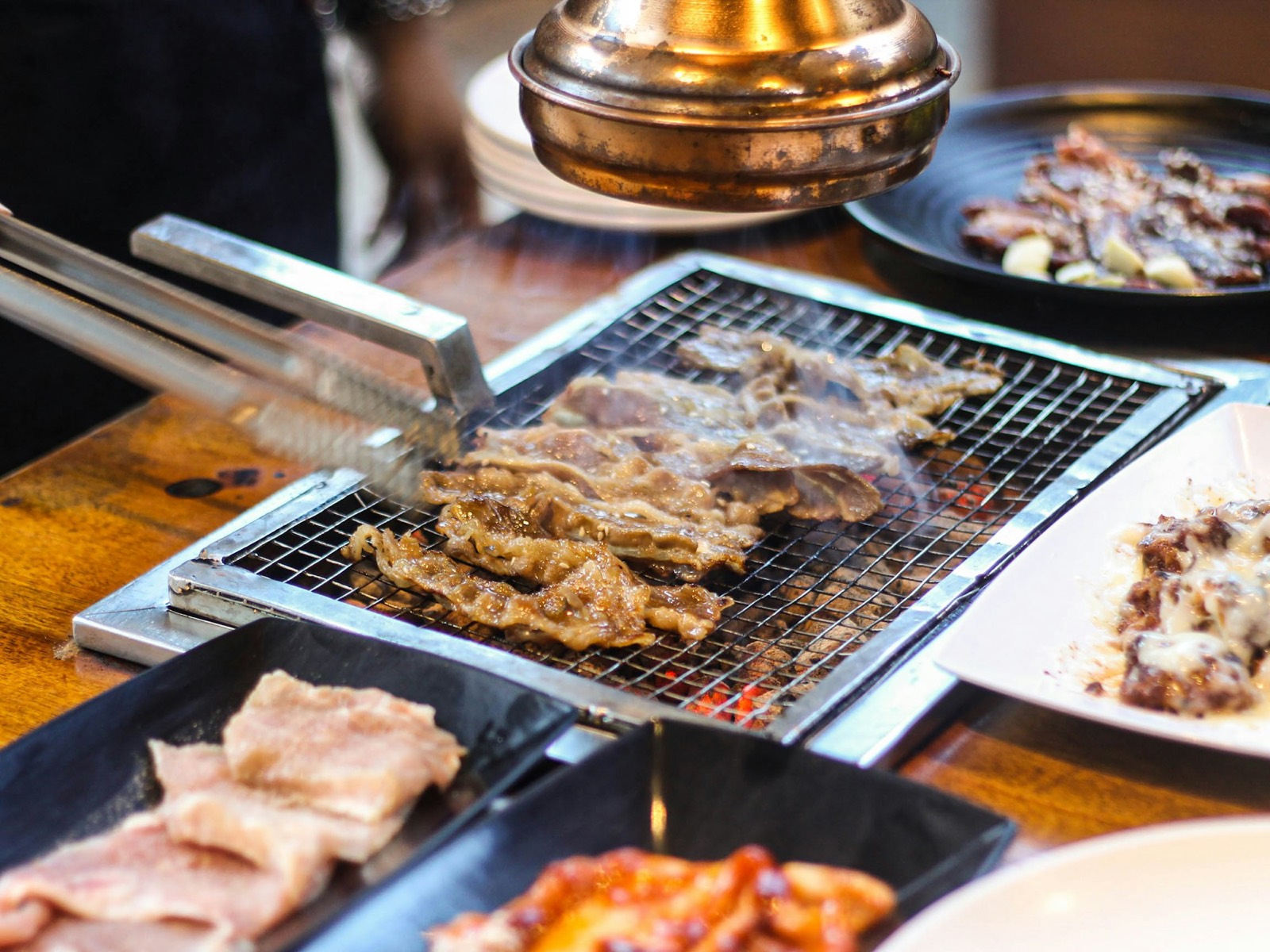 Vlees wordt met een tang omgedraaid op een grill aan tafel